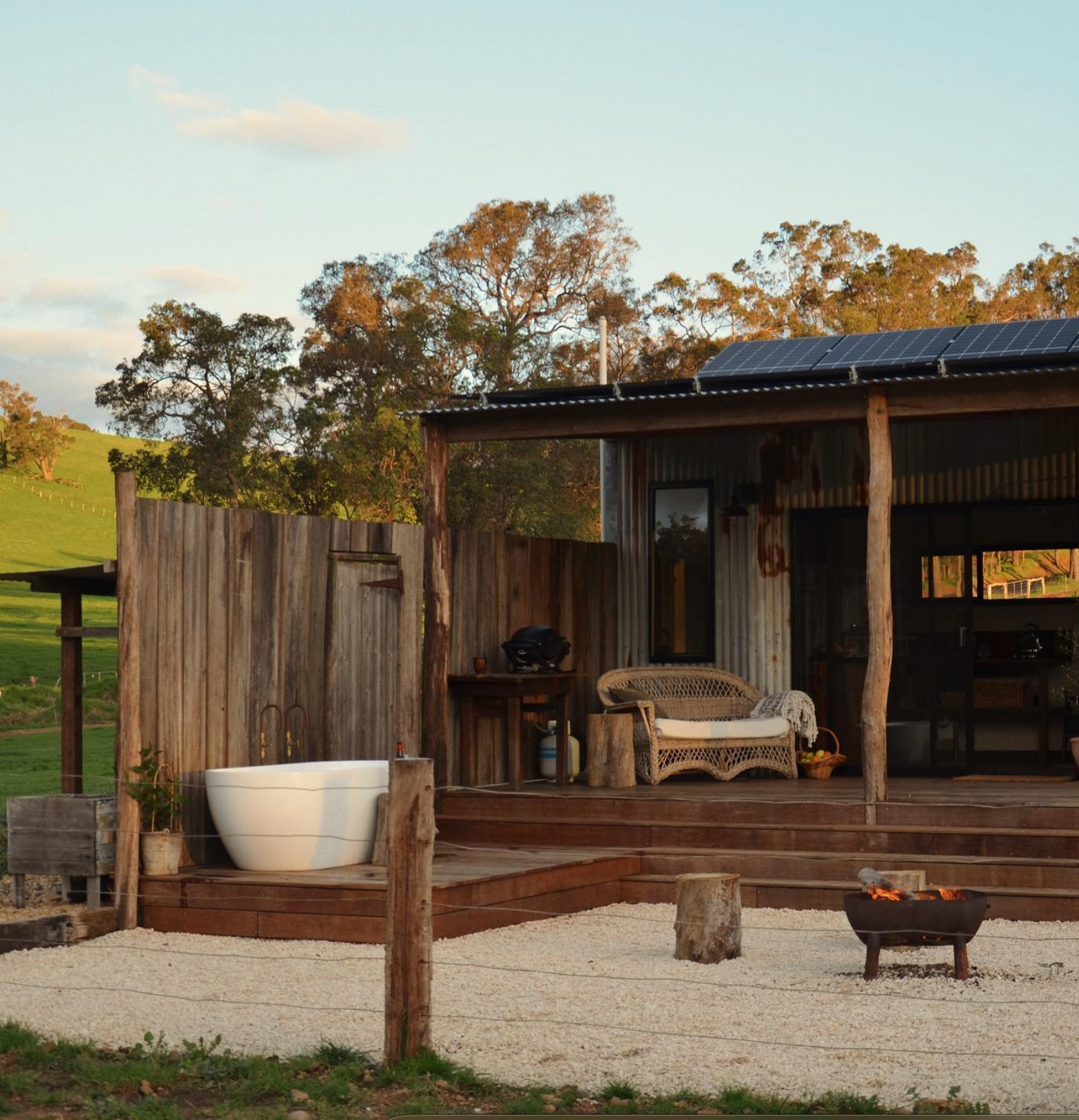 Rustic outdoor bathroom with freestanding tub on wooden deck overlooking countryside.