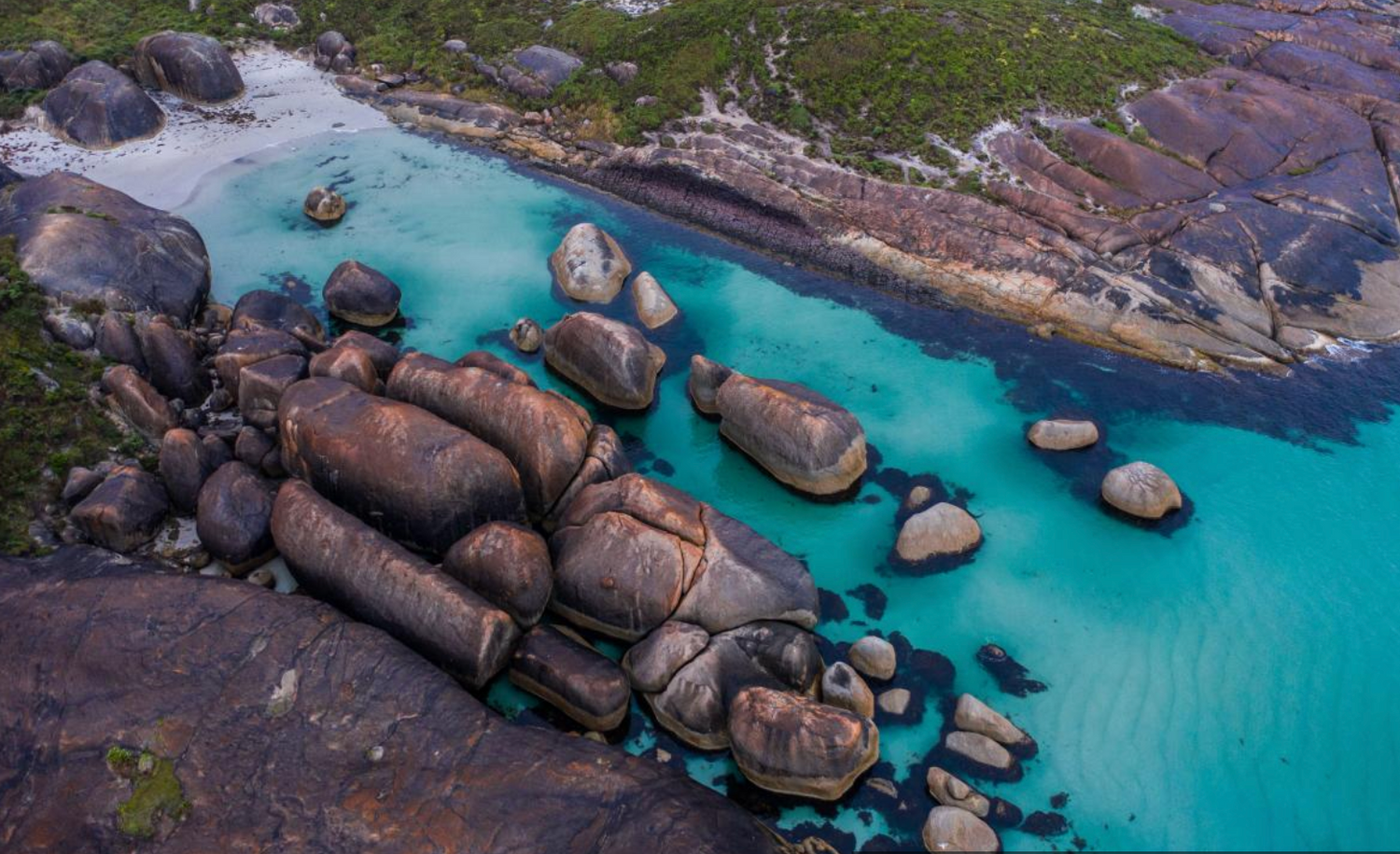 Aerial view of turquoise waters surrounding large granite boulders in coastal cove.