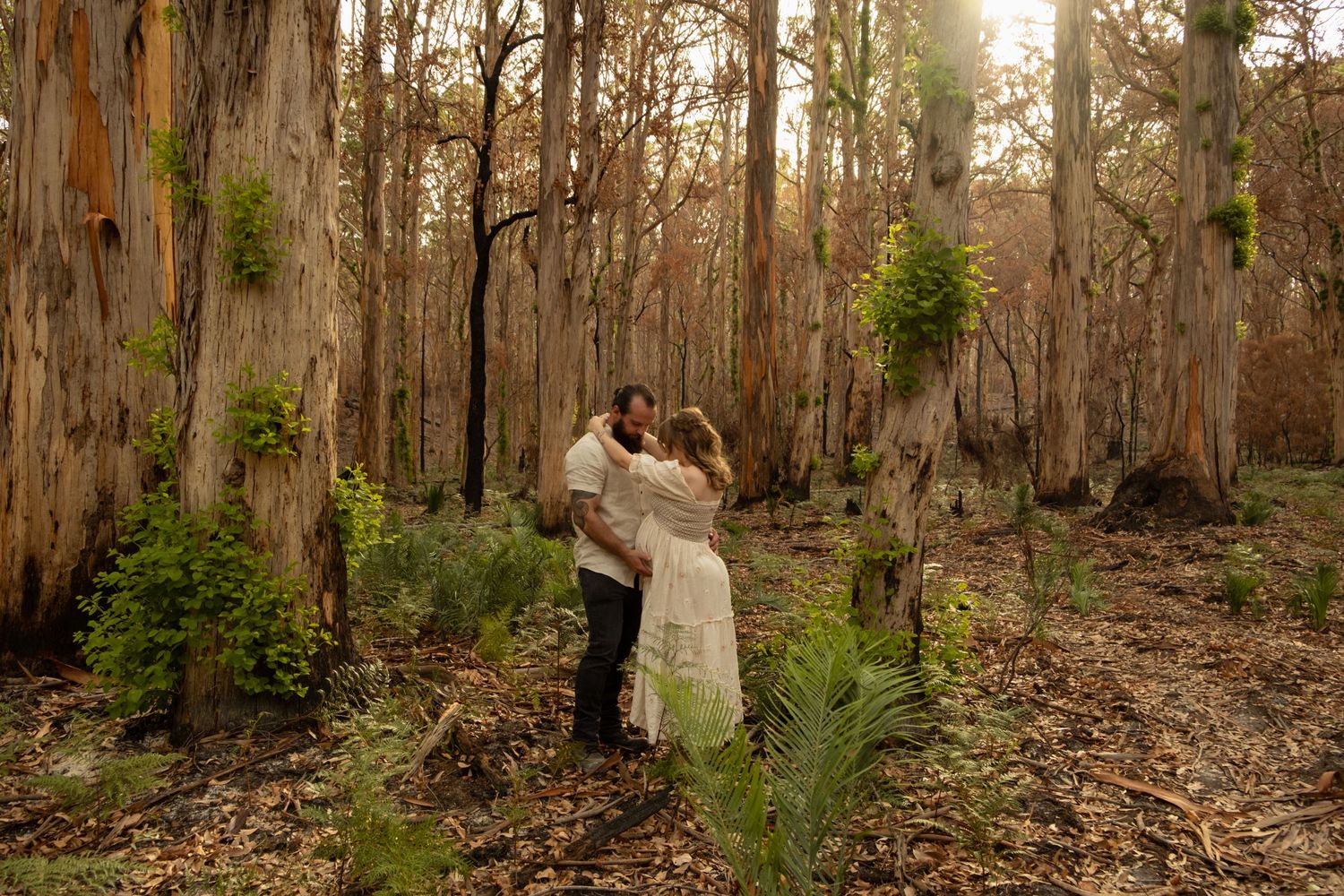 Romantic couple embracing in misty eucalyptus forest during golden hour.