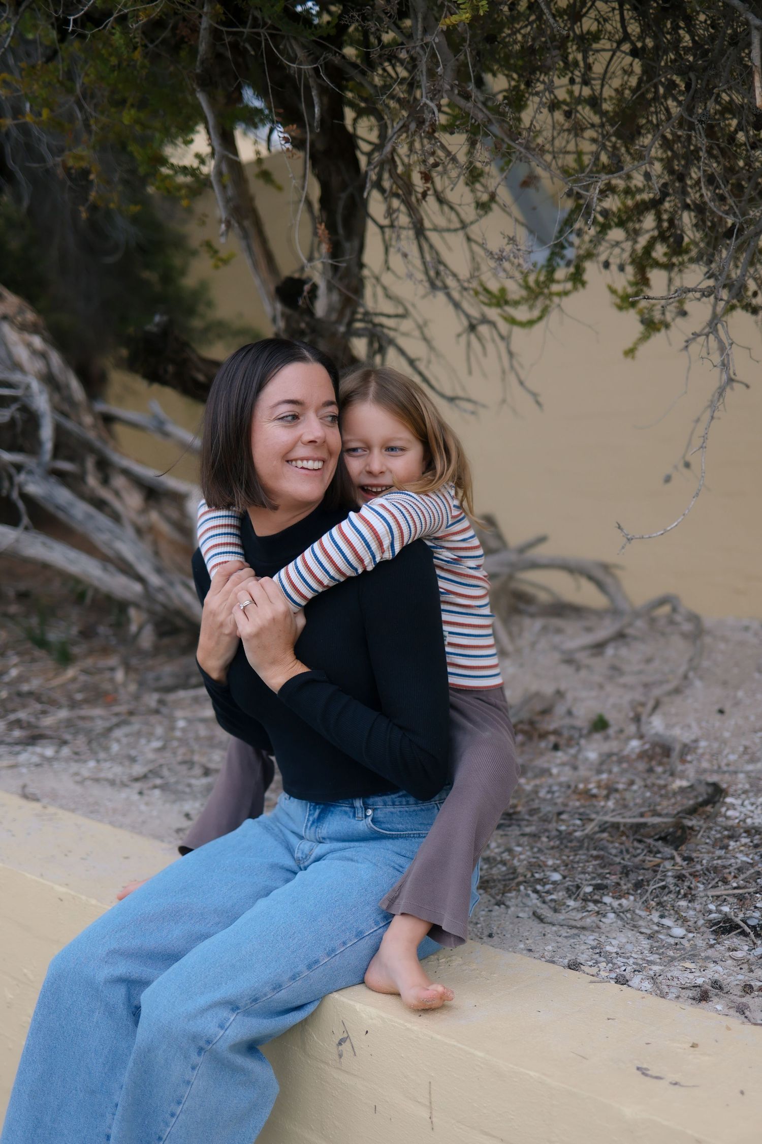 A loving embrace shared between two people wearing striped shirts sitting outdoors near a tree.
