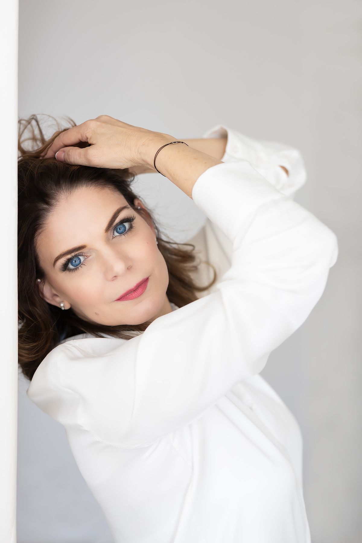 Person in a white sweater poses against light gray background wearing delicate jewelry and natural makeup.