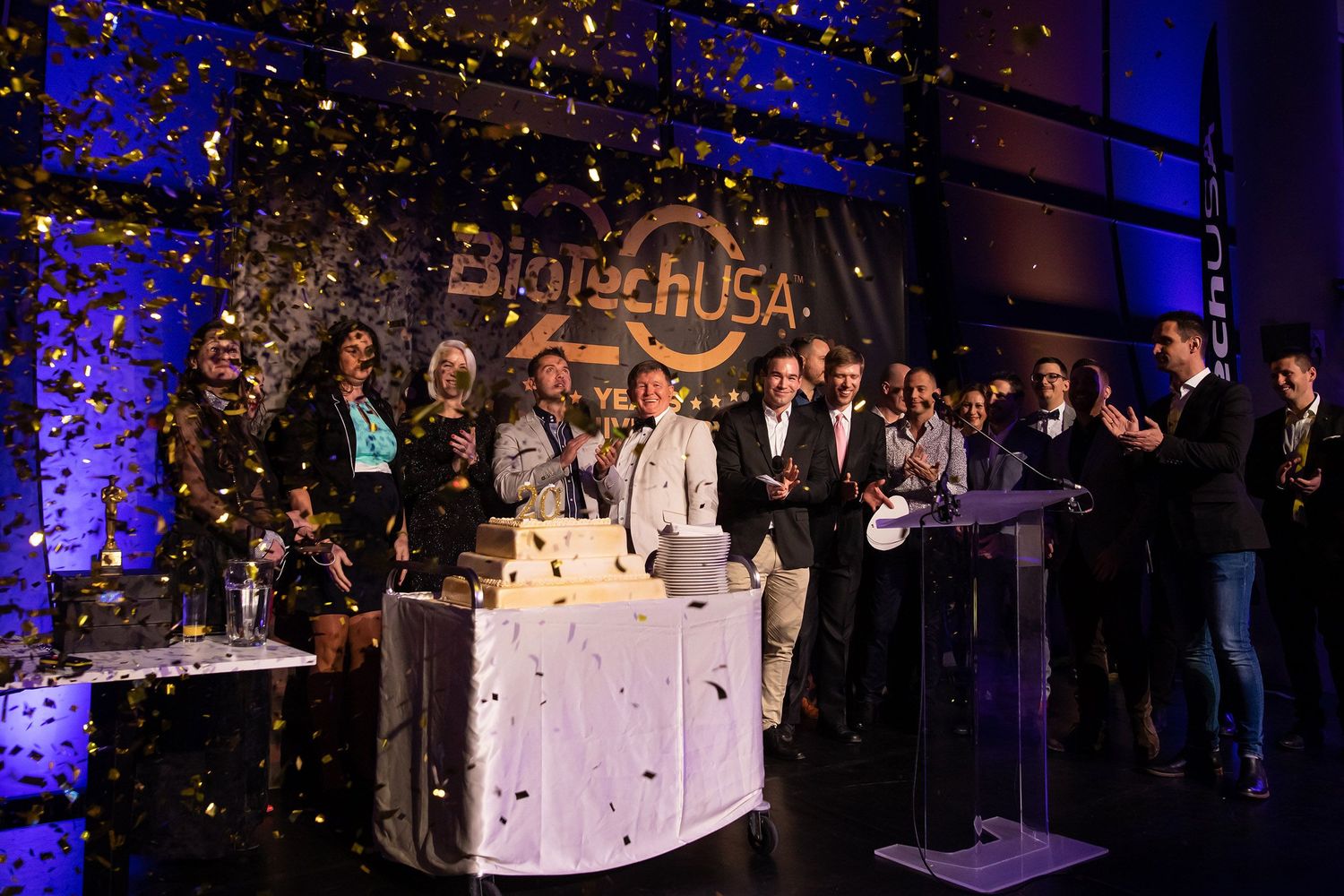 A group stands at a gala event with blue uplighting and decorative elements on stage during an awards ceremony.