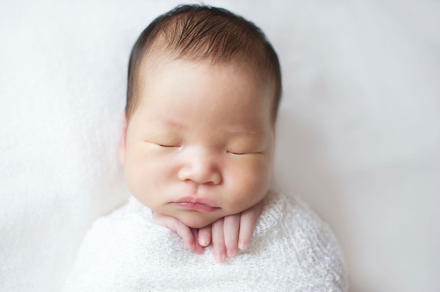 Close-up of a peacefully sleeping newborn wrapped in a white swaddle, photographed by Phoebe Lee Photo in Toronto