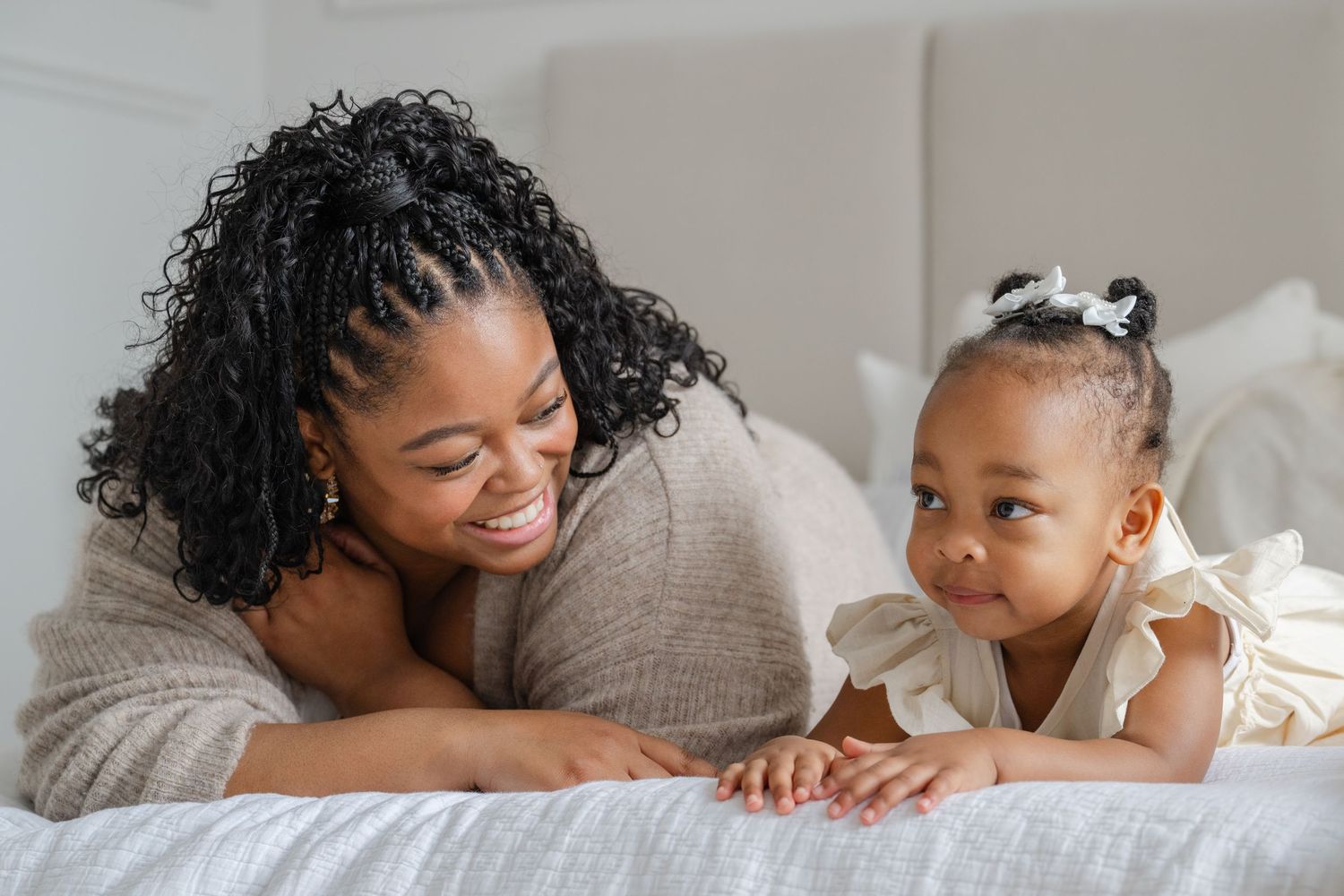 A tender moment between mom and child as they cuddle together on the bed and share gentle smiles. Family photo session by Phoebe Lee Photo.