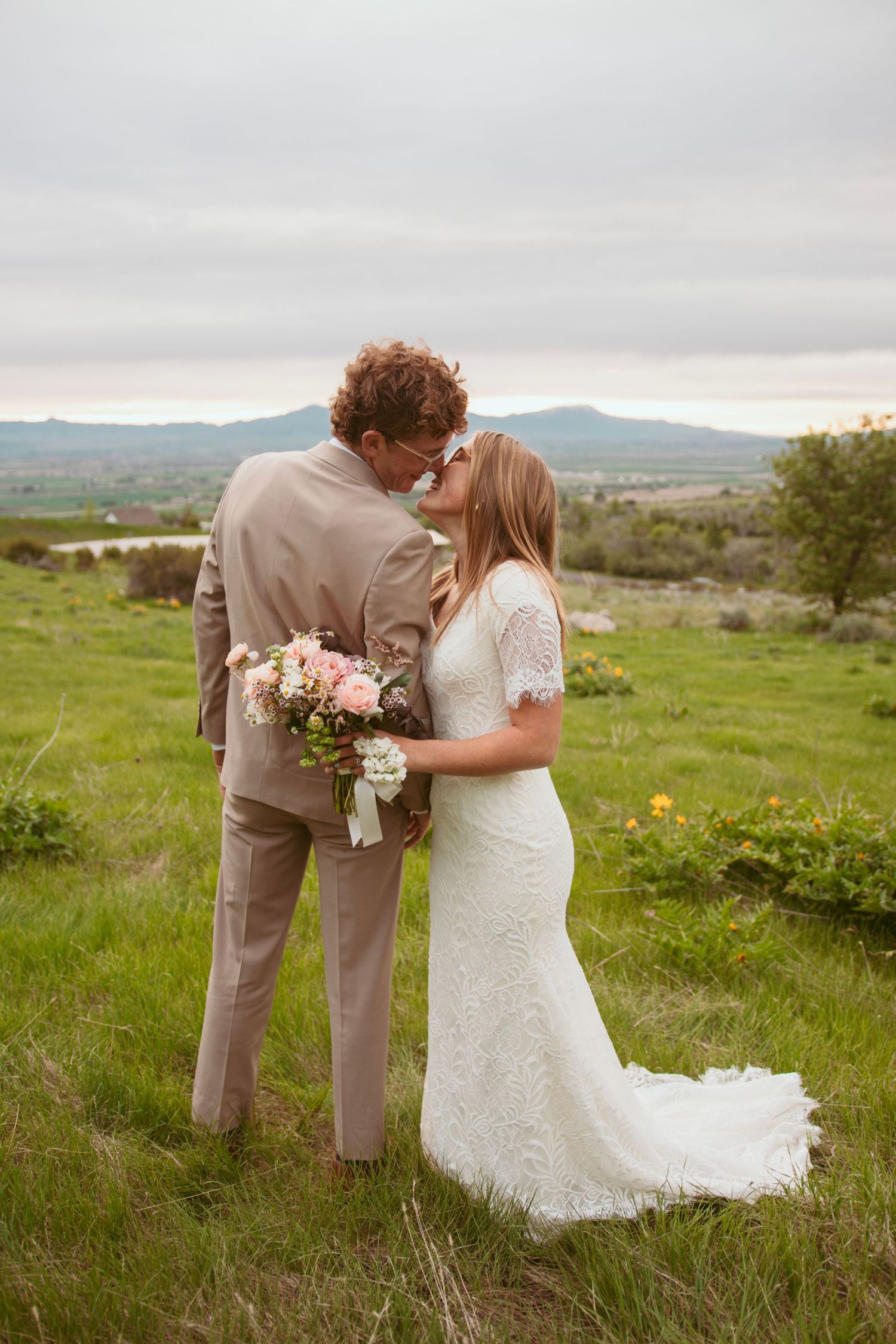 A romantic outdoor wedding moment set against a scenic mountain view with a pink rose bouquet in the countryside.