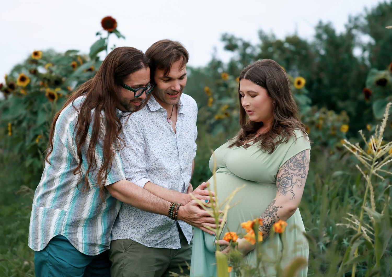 Three friends share a tender moment in a sunflower field as they celebrate an upcoming arrival during a maternity photo session.