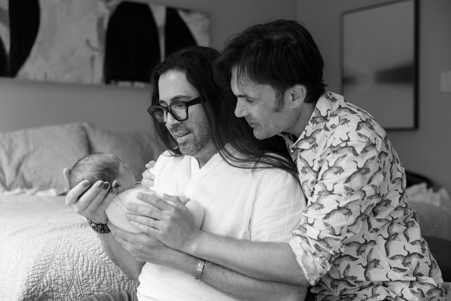 Black and white photo showing a couple sharing a tender moment with their newborn baby on a bed.