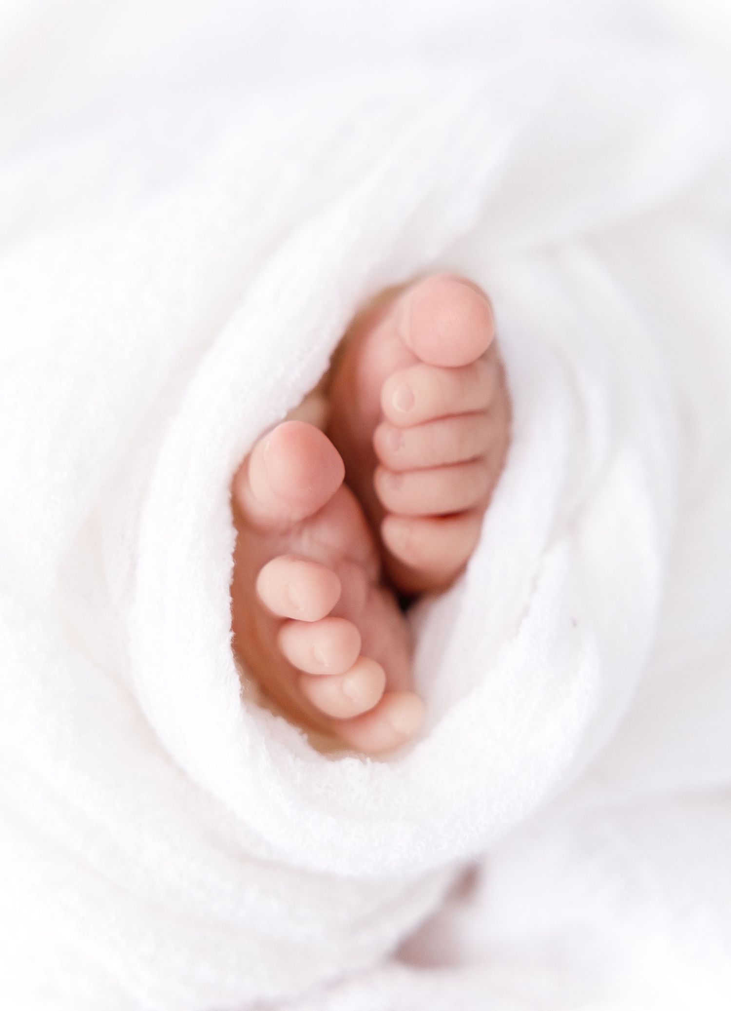 Tiny baby feet peek out from soft white blanket folds in a tender newborn photograph.