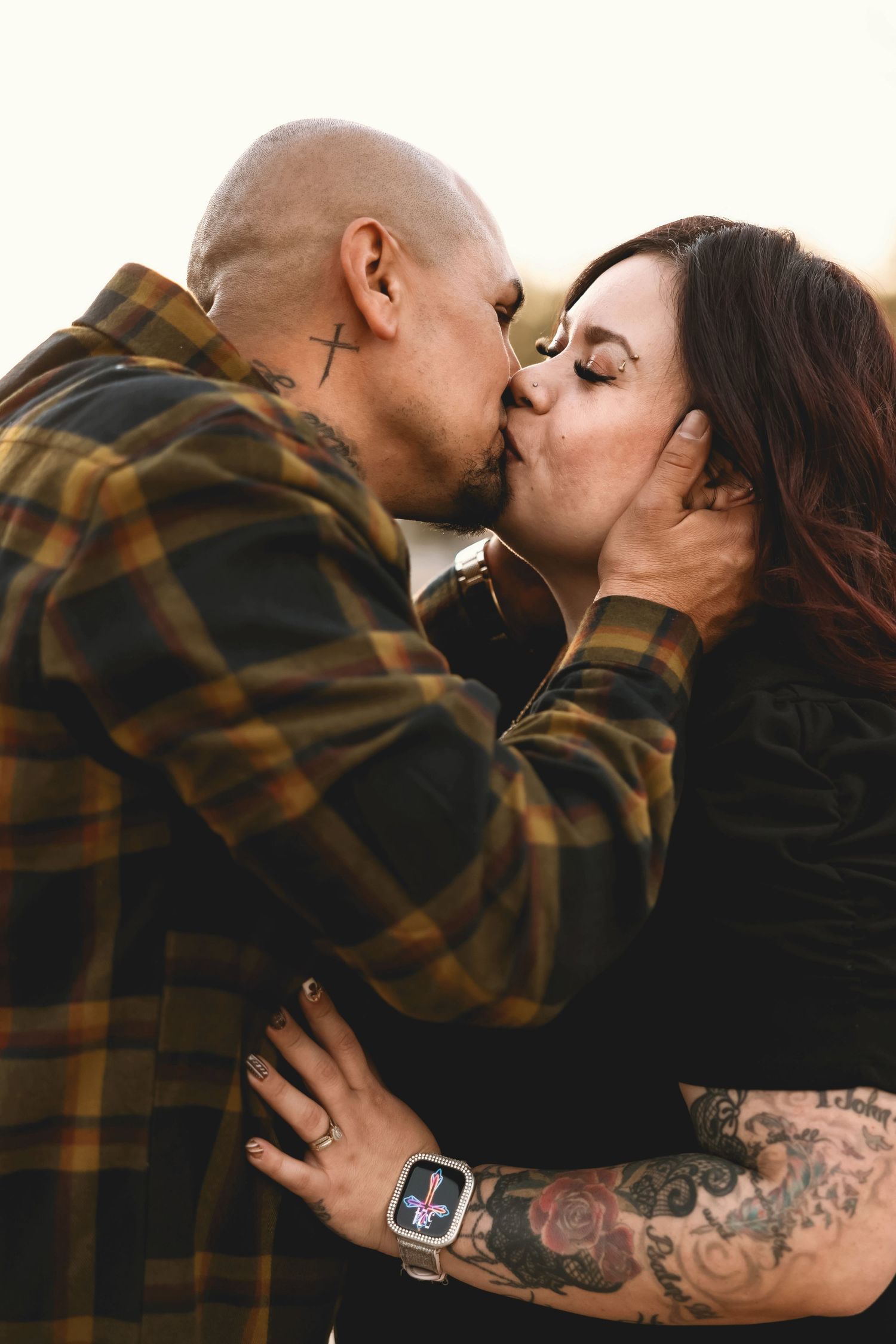 Intimate kiss between couple wearing plaid and black during sunset photoshoot.