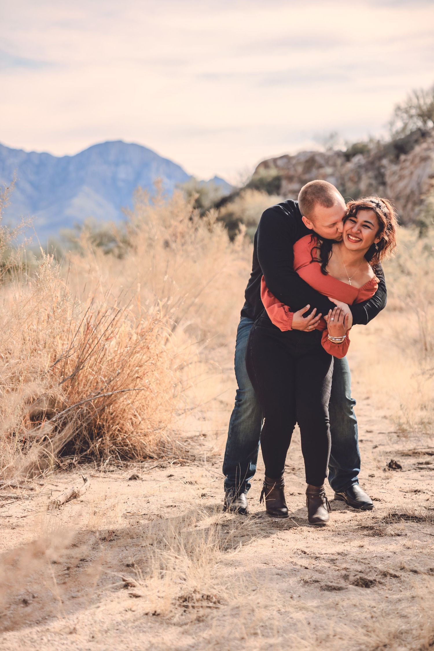 Affectionate couple embracing on a desert trail with mountains in the background.