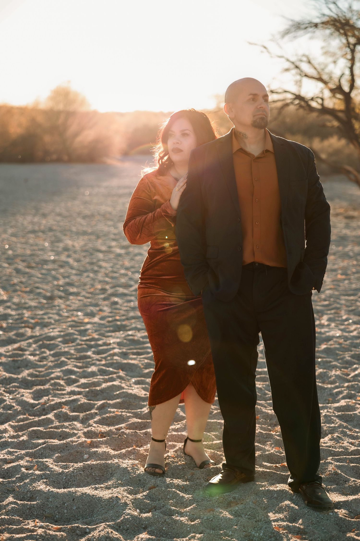 Couple stands together on sandy terrain during golden hour photo session.