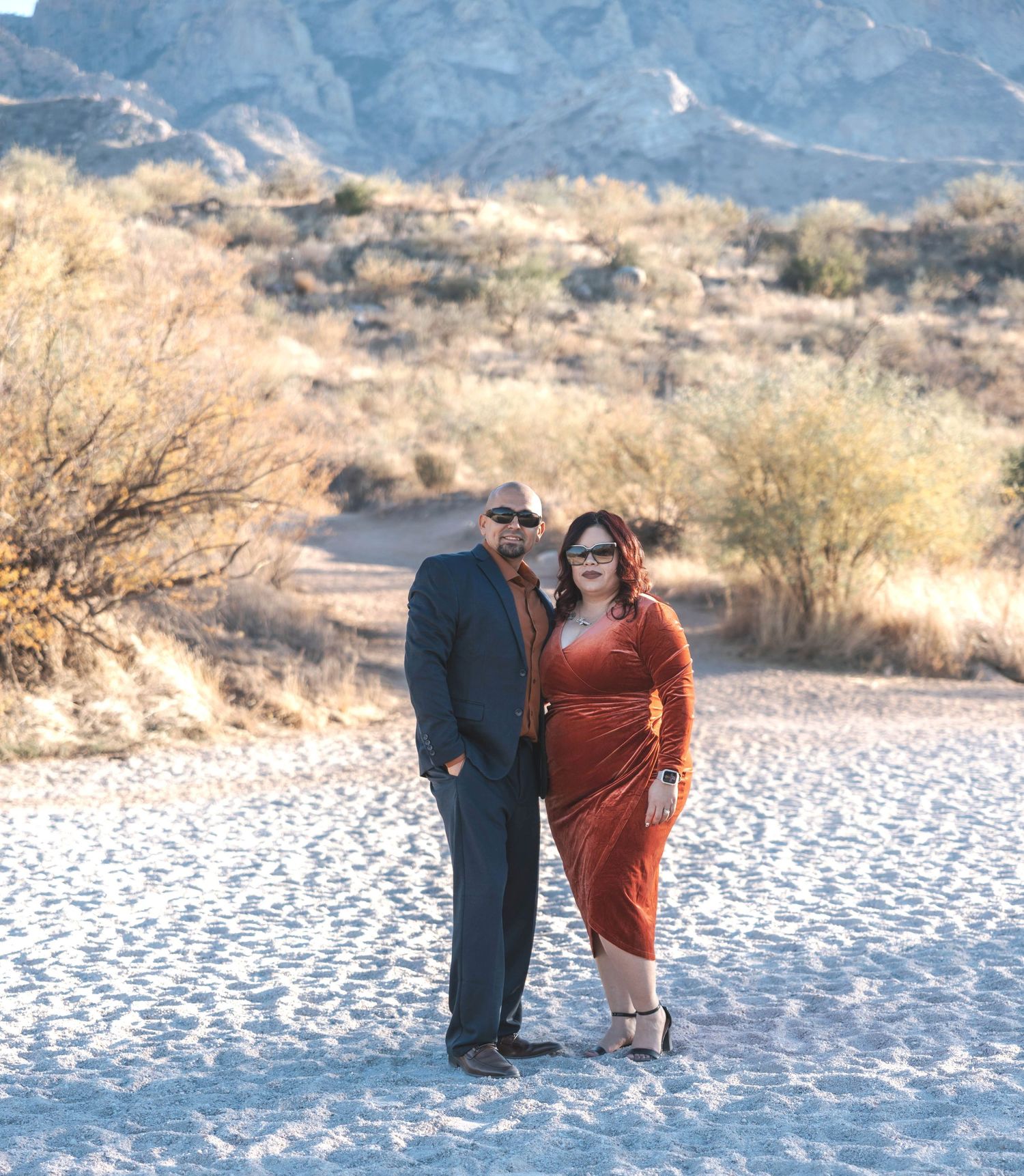 Couple poses together on a desert path with snow-capped mountains in the background.