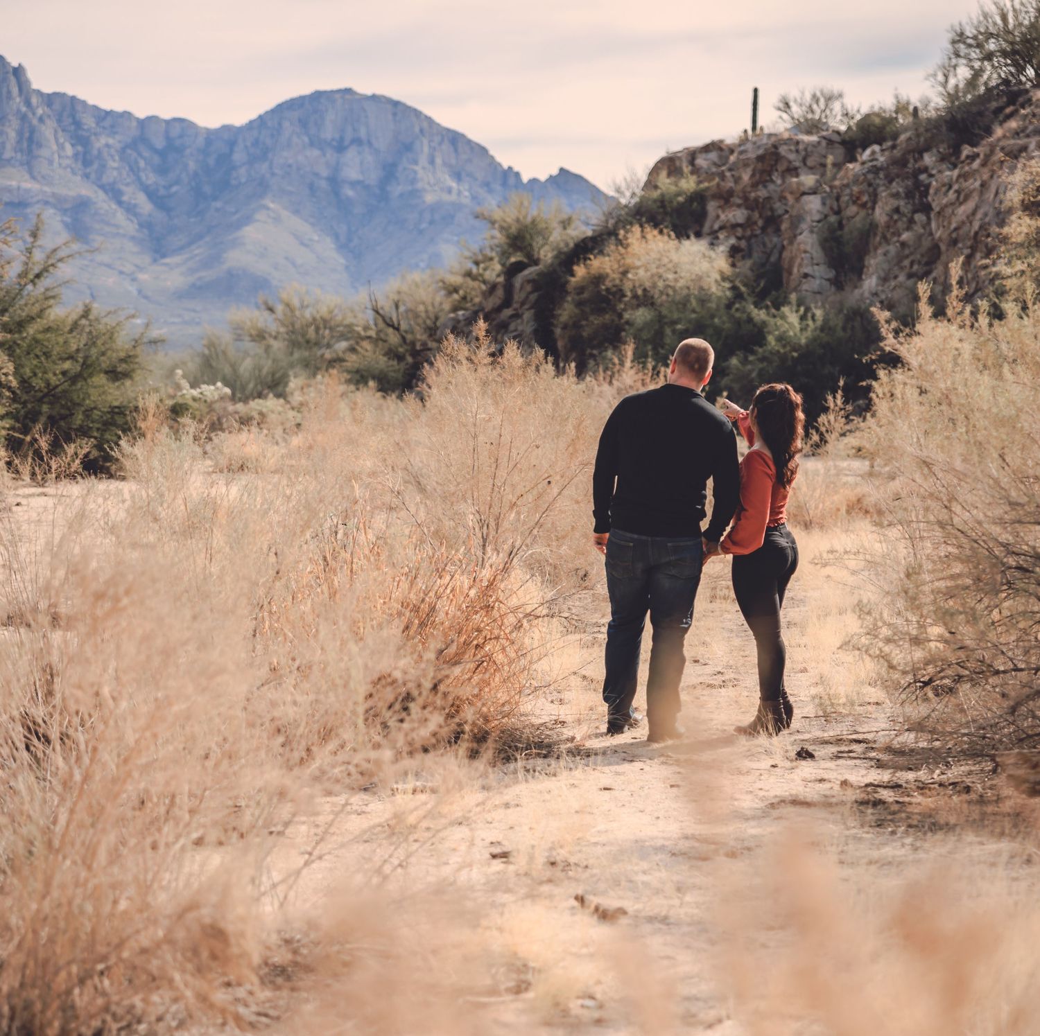 Couple hiking on a desert trail with dramatic mountain views in the background.
