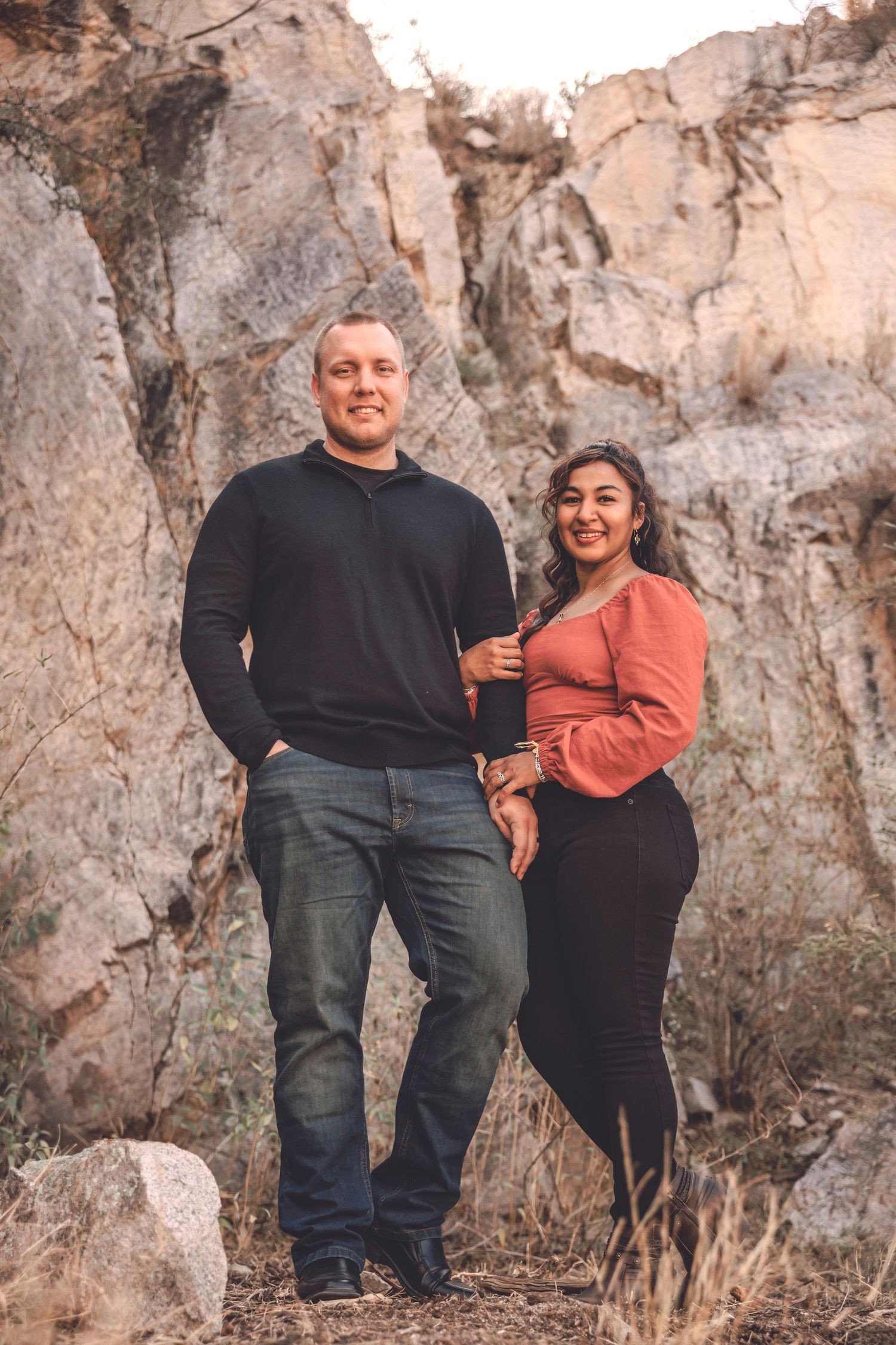 Couple posing together against a dramatic rocky cliff backdrop in the desert.