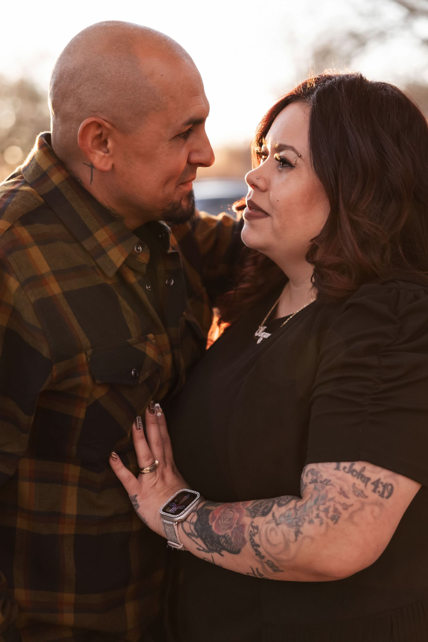 Couple shares romantic moment in black and plaid outfits during sunset.