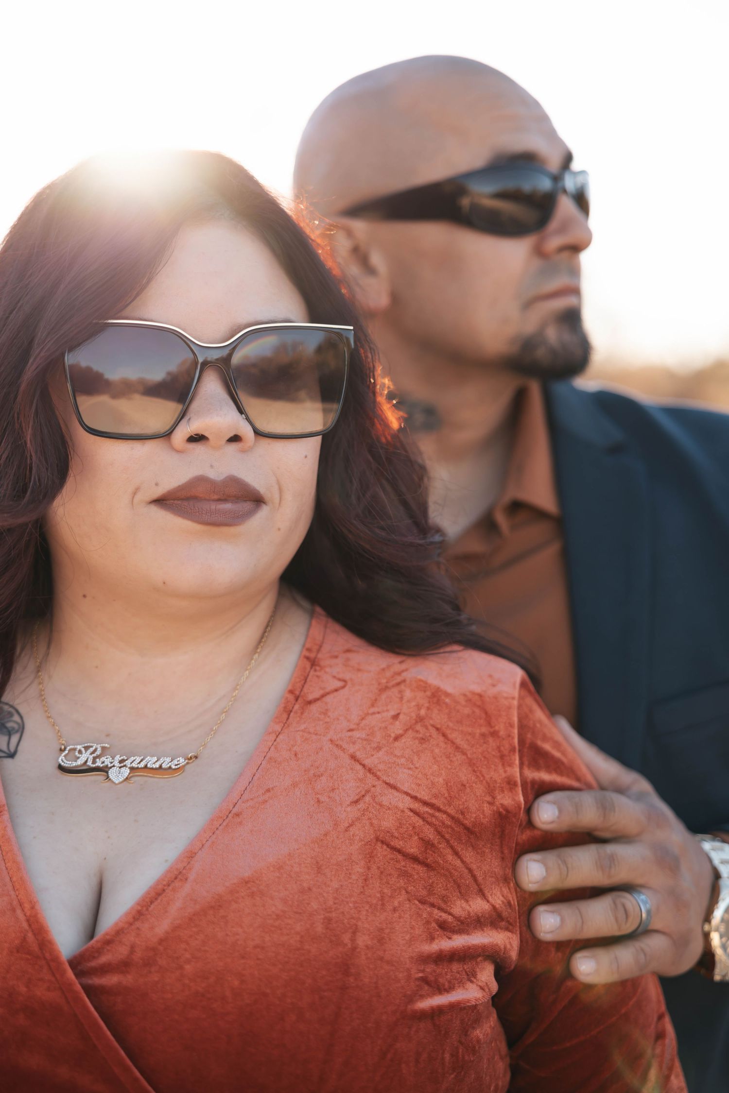 Couple wearing sunglasses pose together in warm sunset lighting.
