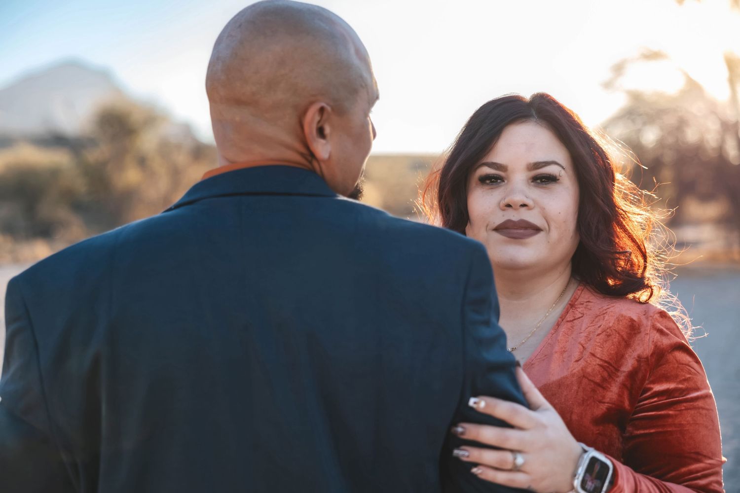Romantic couple embraces during sunset photoshoot with desert mountains in background.