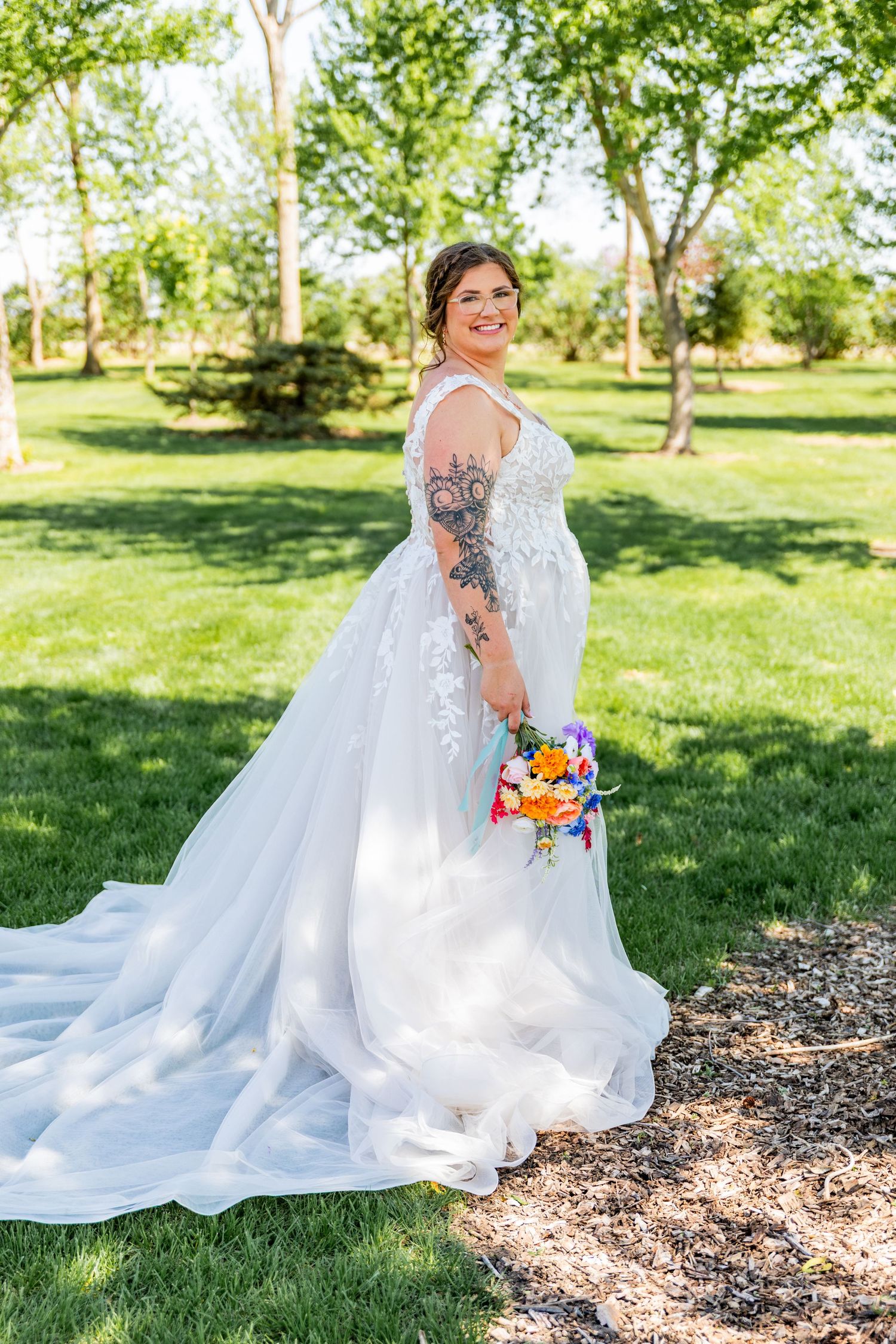 A wedding dress flows elegantly across a garden setting with scattered wood mulch and green grass background.
