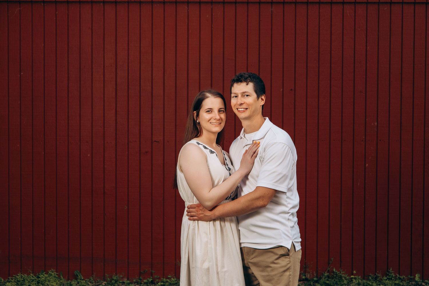 A couple poses affectionately against a red barn wall background.