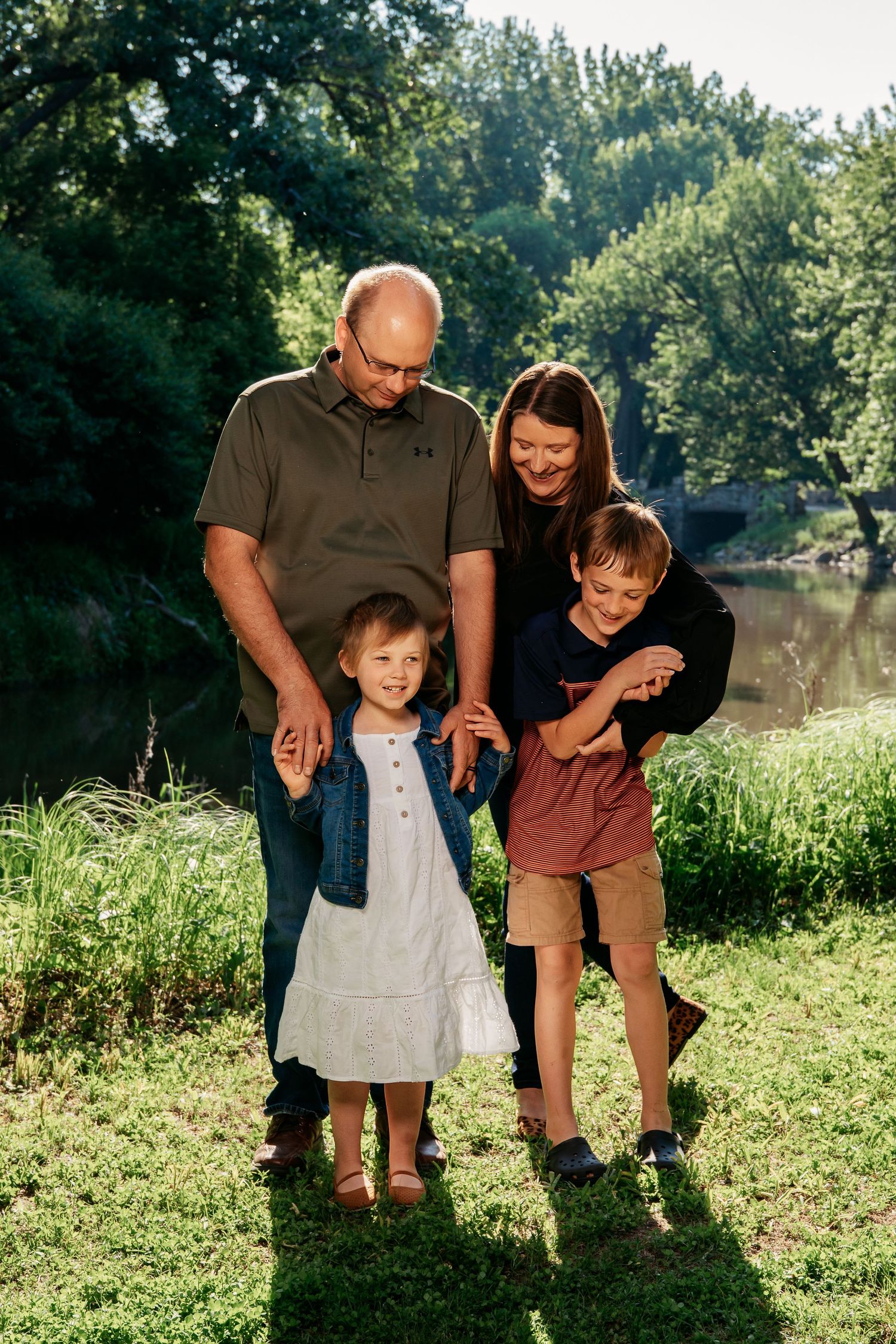 A happy family enjoying a summer day together by a tranquil pond surrounded by lush greenery and trees.