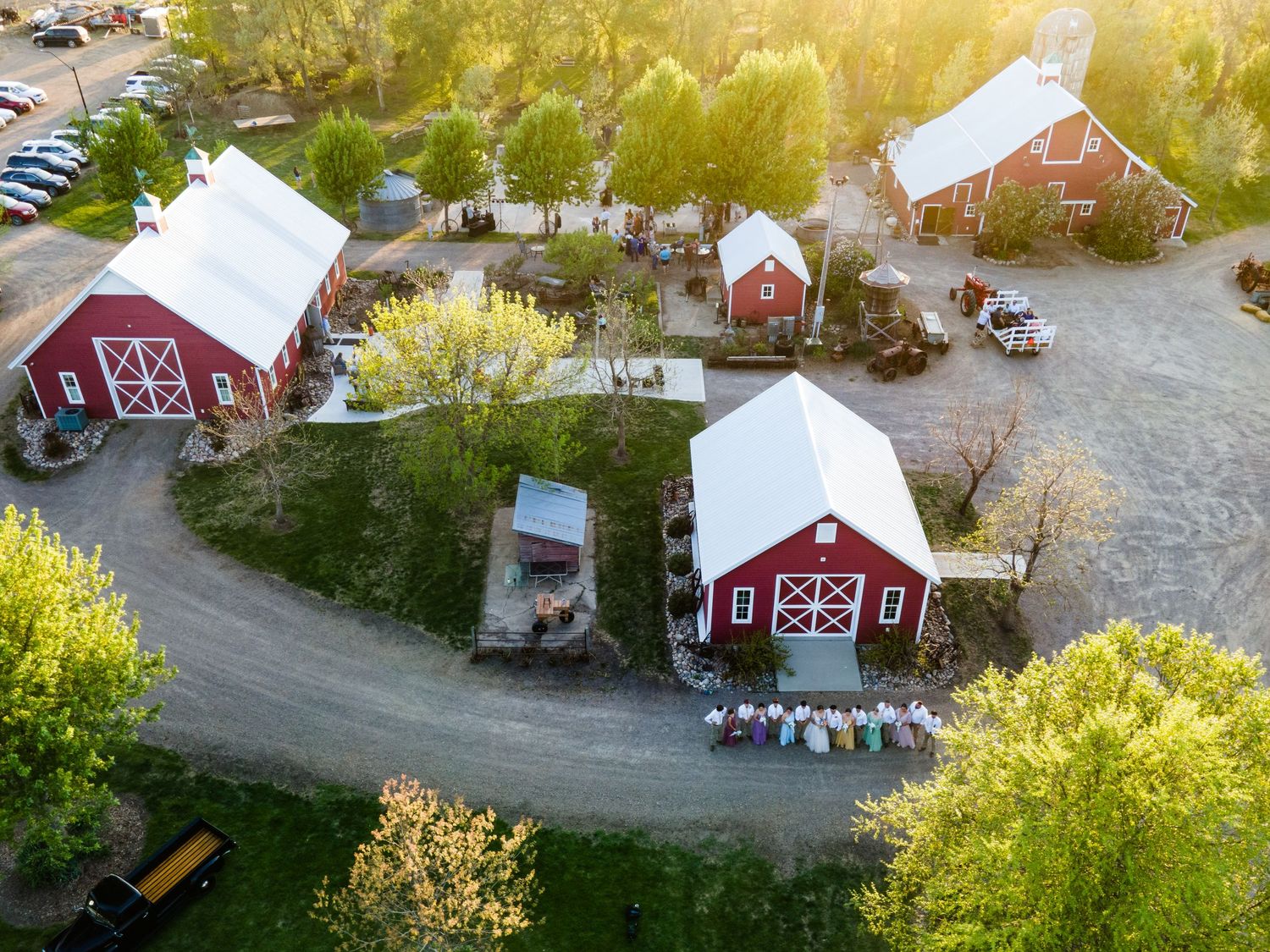 Aerial view of red barn buildings and parking area at rustic farm venue during golden sunset.