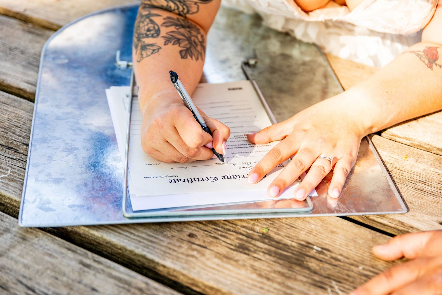 Close-up of hands signing wedding documents on a rustic wooden surface.