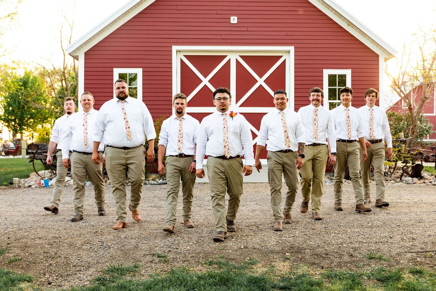 Groomsmen in matching white shirts and khakis pose casually in front of a red barn.
