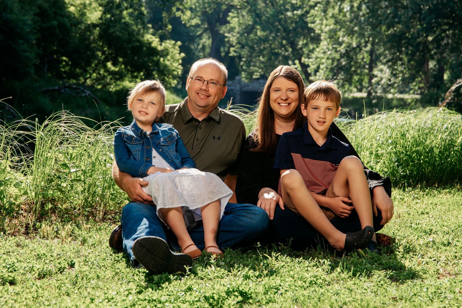 A family sitting together on grass in a sunny park setting with natural greenery in the background in Montevideo Minnesota