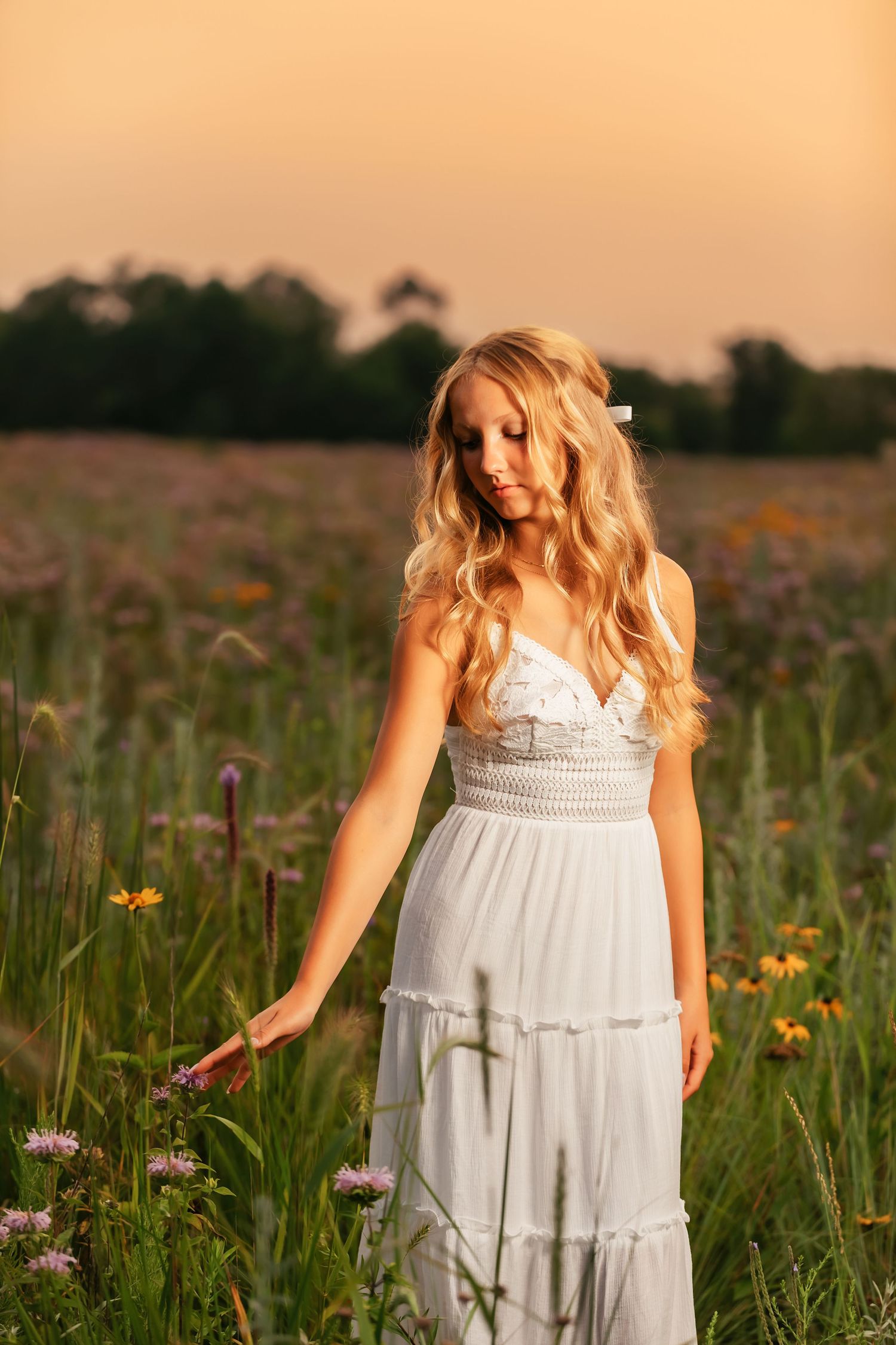 A white sundress catches golden light in a wildflower meadow during sunset.