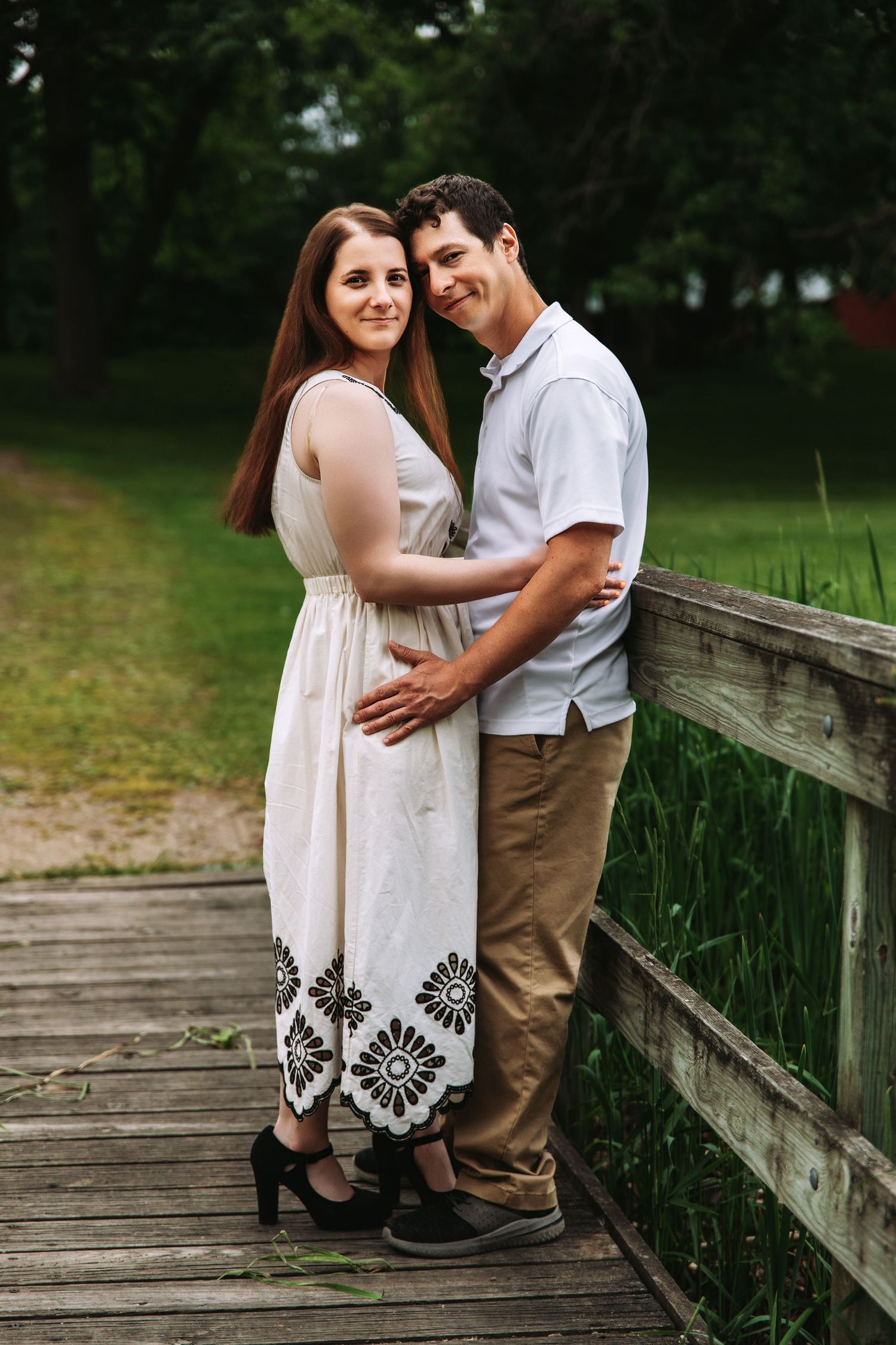 A romantic couple embraces on a wooden boardwalk surrounded by lush greenery on a summer day.