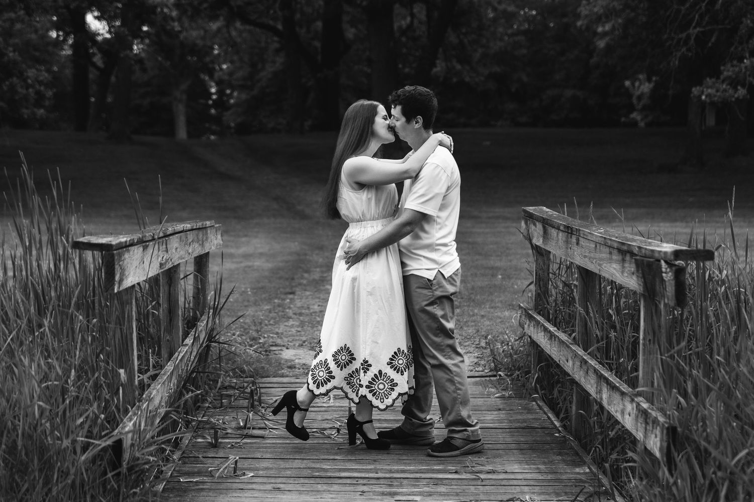 A romantic couple sharing tender moments on a wooden boardwalk in black and white.