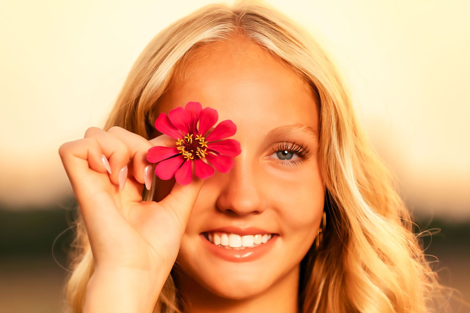 A bright pink zinnia flower is held up against a warm sunset background.