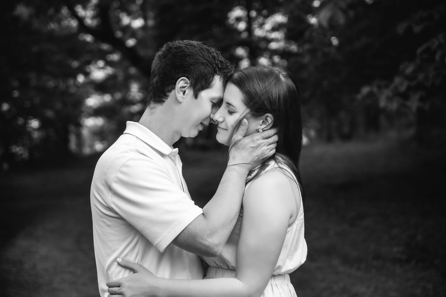 A black and white portrait of a couple sharing an intimate moment in a wooded park.
