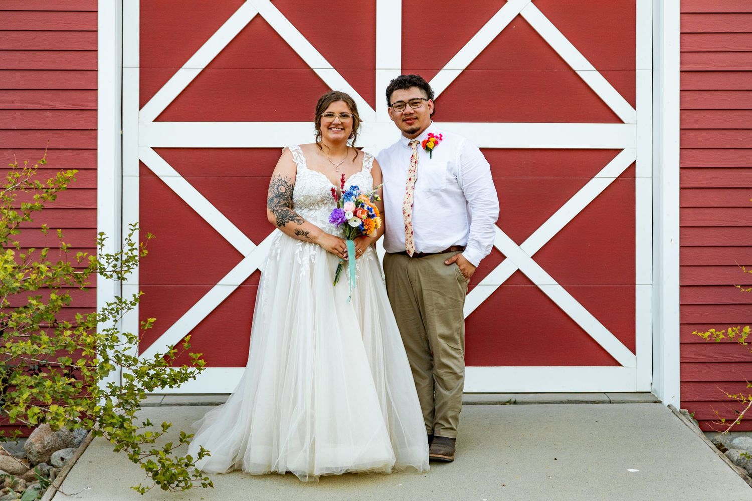 Red barn with white trim serves as backdrop for rustic wedding photography.