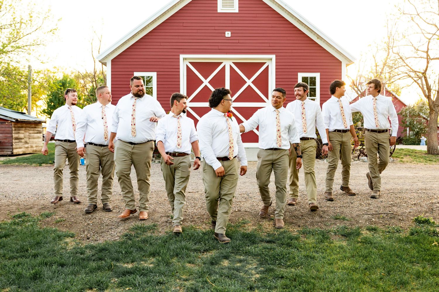 A group in white shirts and khaki pants poses in front of a classic red barn with white trim on a sunny day.