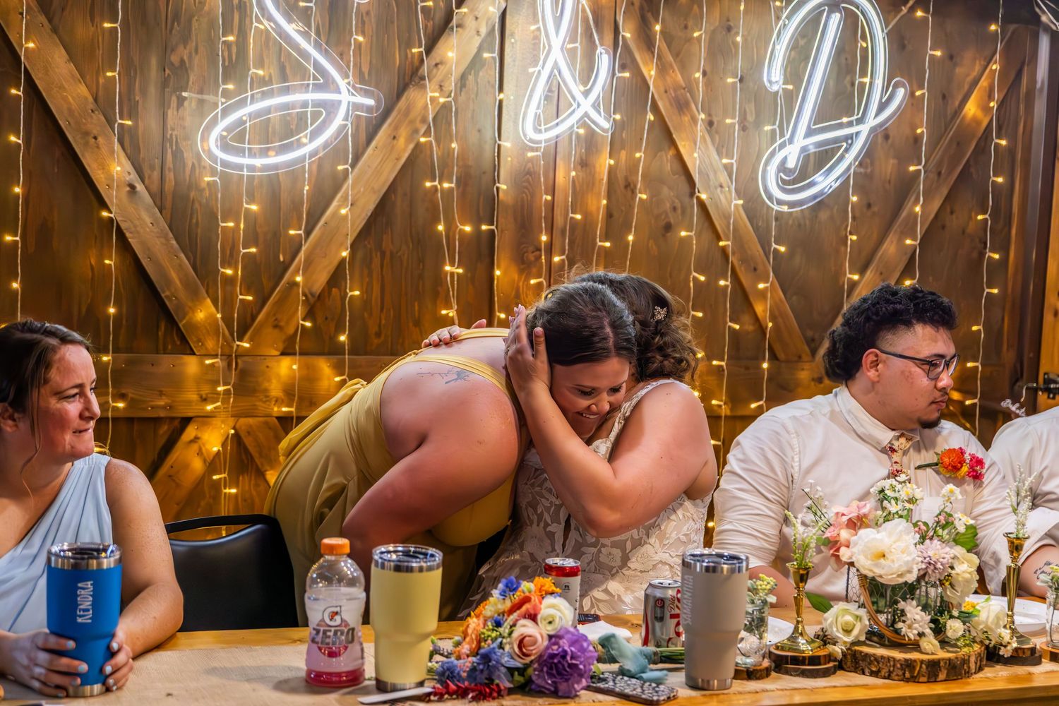 Wedding reception table with neon lights and string lights creating warm ambiance in rustic barn setting.