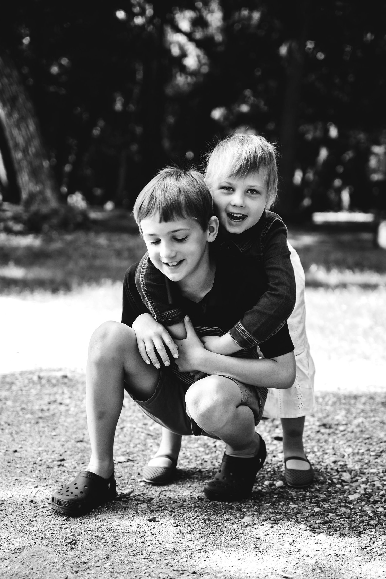 Black and white candid photo of two children playing and laughing together outdoors.