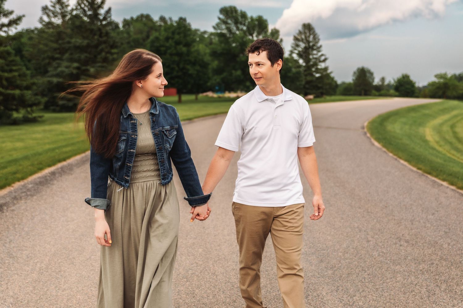A couple walking hand in hand on a curved gravel path surrounded by lush green landscaping.