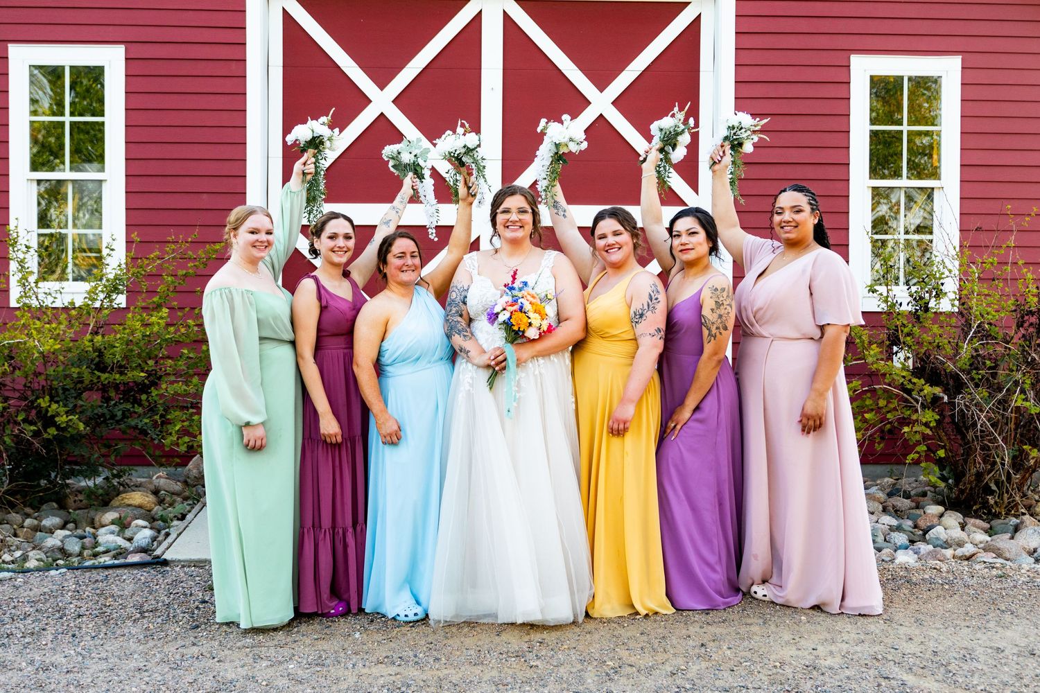 Wedding party in colorful pastel dresses posing in front of a bright red barn.