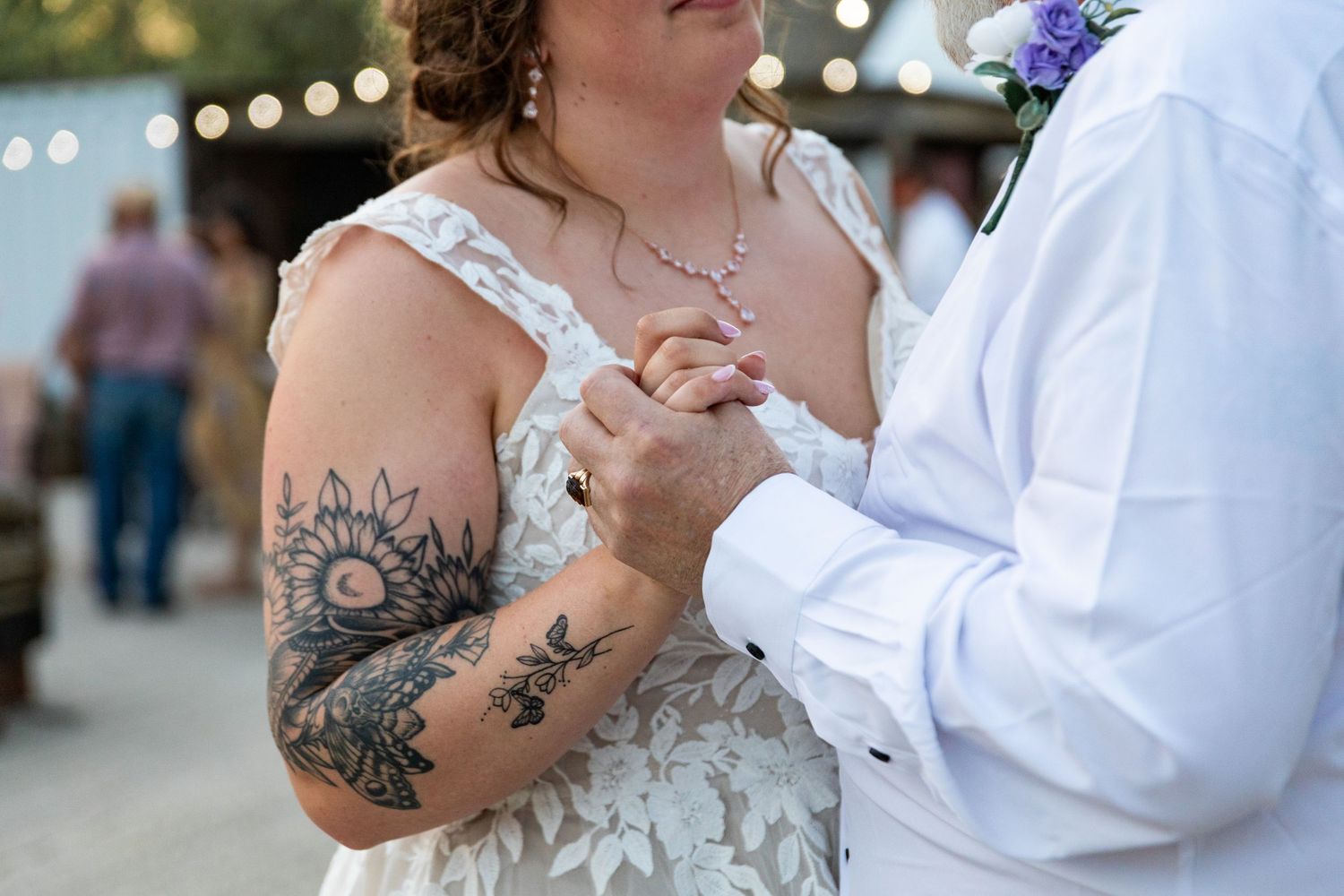 Close-up of couple's hands during first dance, showing bride's floral tattoo sleeve.