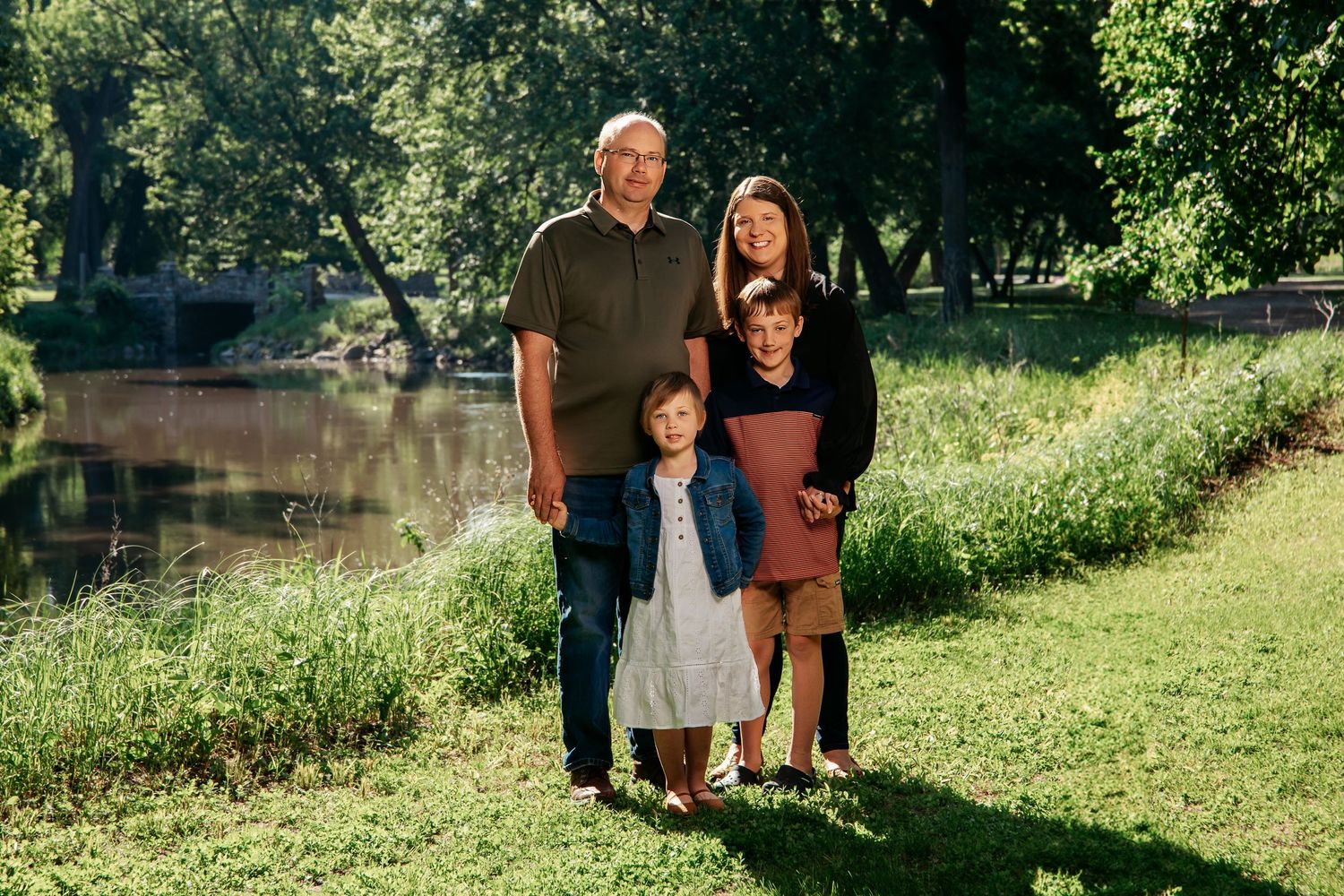 A group stands together on green grass near a tranquil pond on a sunny summer day.