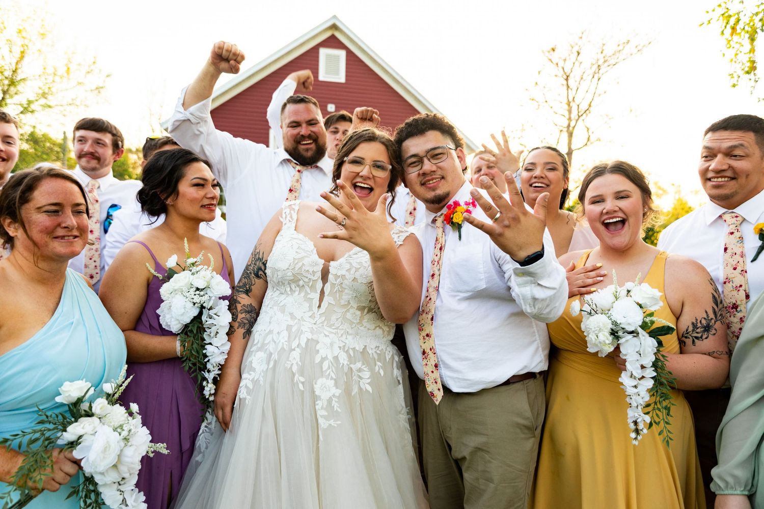 Joyful wedding party celebrating outdoors with a red barn in the background.