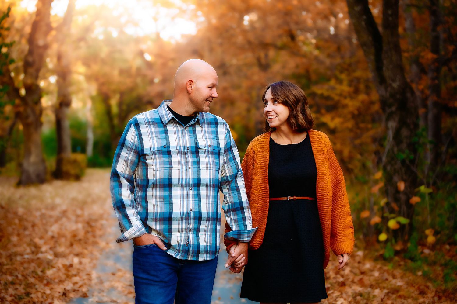 A couple walks hand in hand on a leaf-covered path during golden hour in an autumn forest in Granite Falls Minnesota