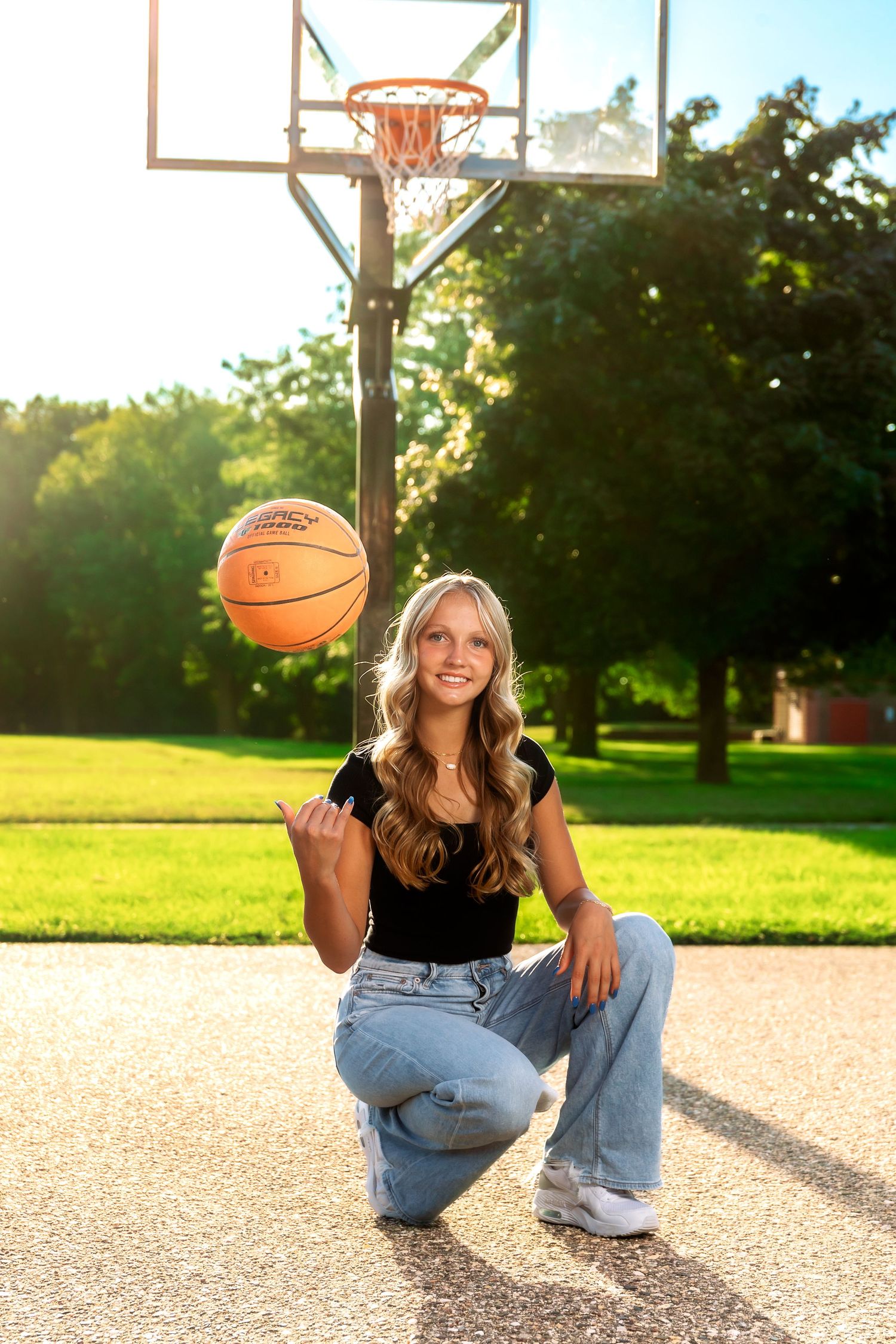 Basketball player posing with orange ball on outdoor court at golden hour.