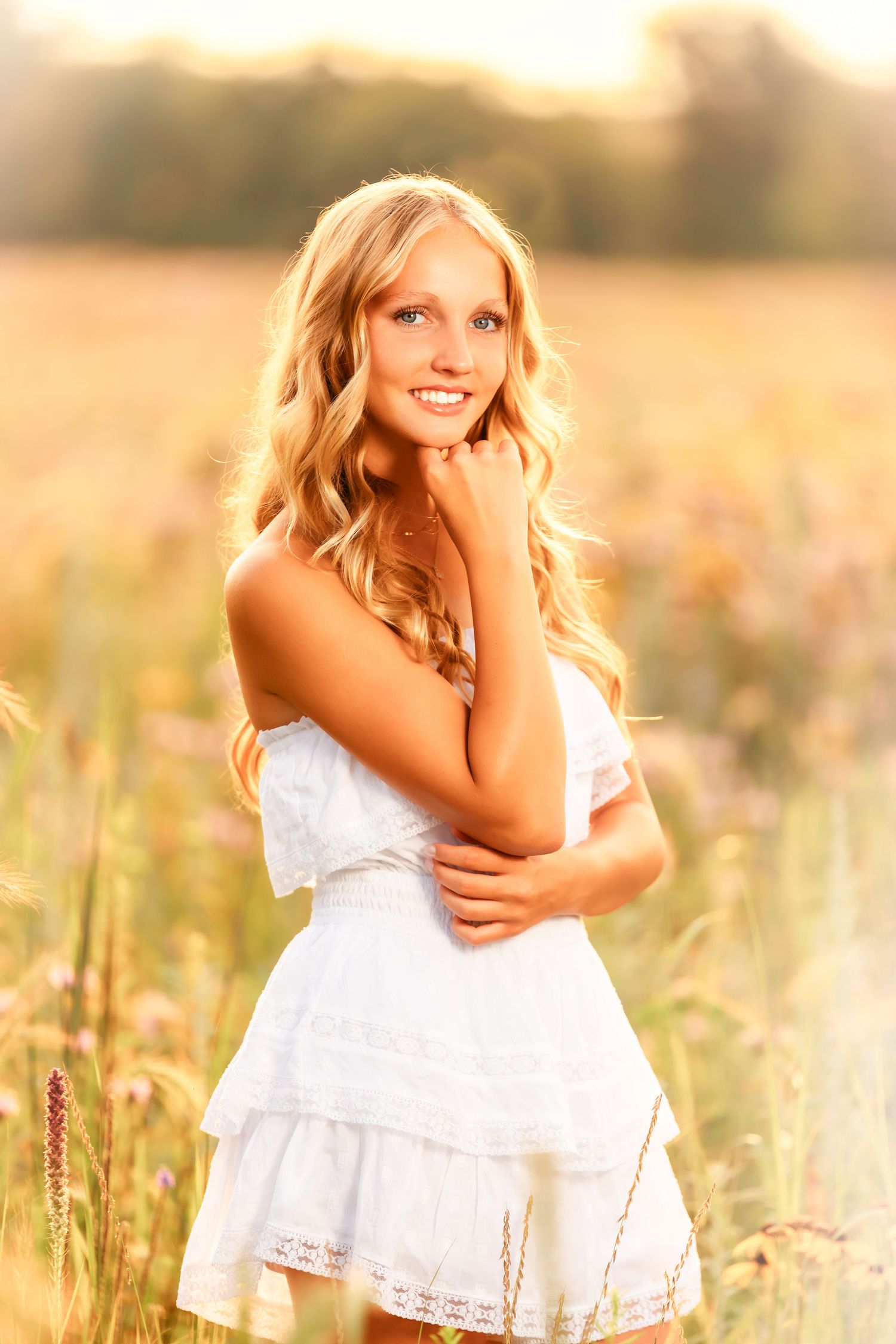 Young girl in white dress playing and laughing in golden sunlit field during sunset.