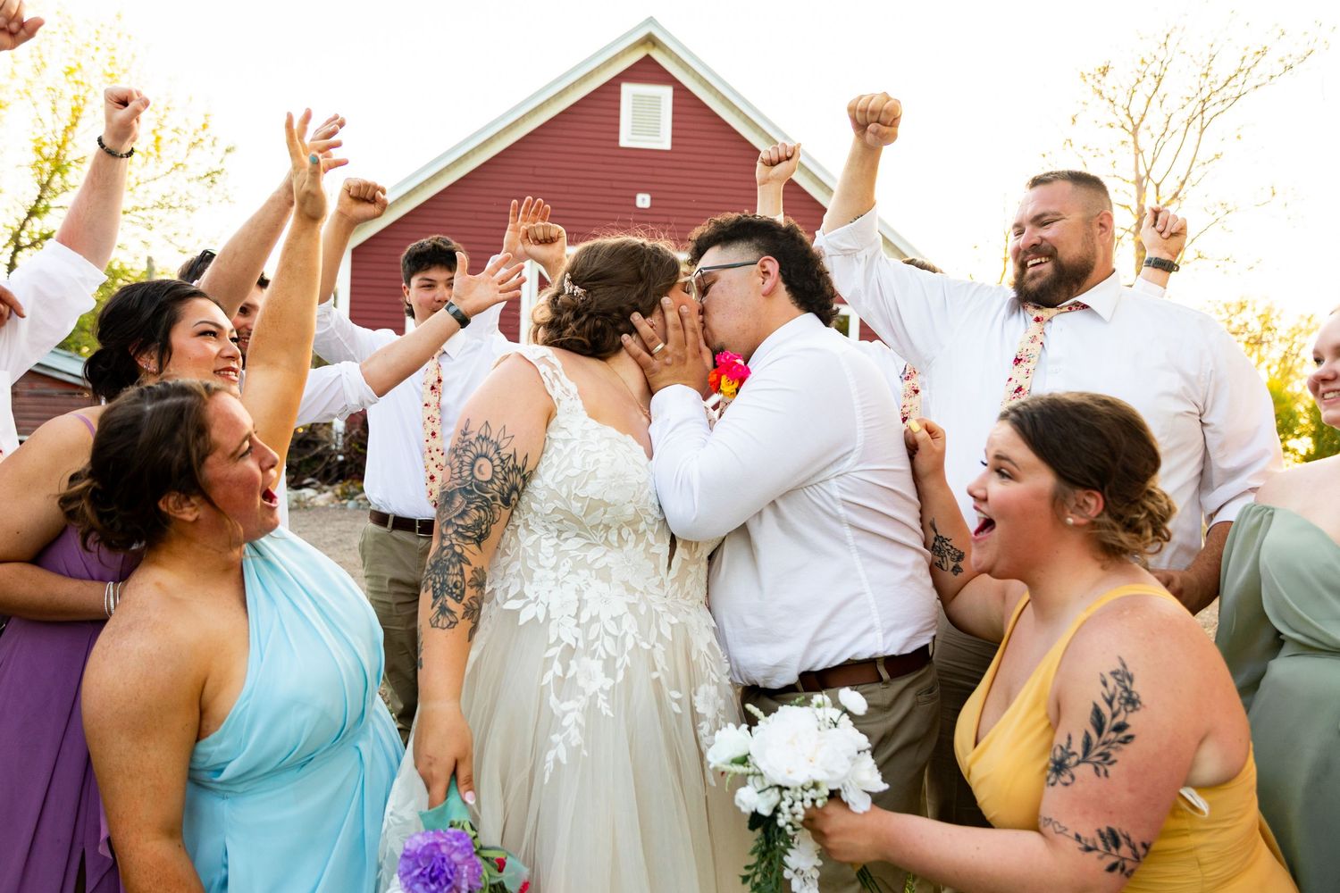 Joyful wedding party celebration shot with everyone raising their arms in front of barn.