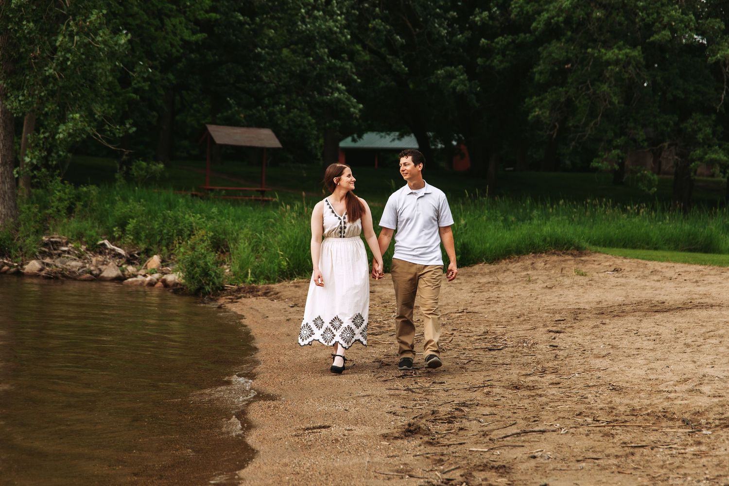 A couple walks hand in hand along a peaceful shoreline beach at dusk.