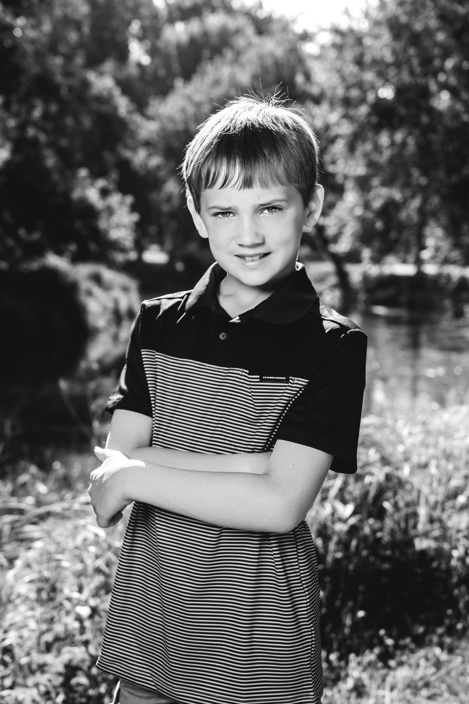 Black and white portrait of a youth in a striped polo shirt standing by a pond in summer.