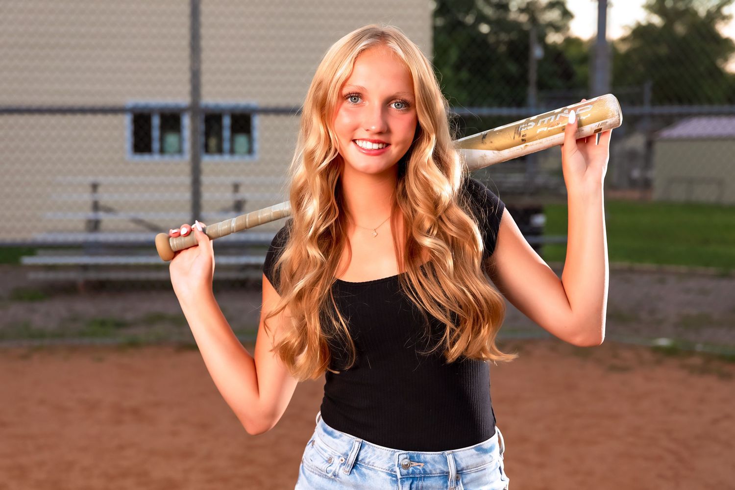 Baseball player holding bat on dirt field during golden hour photo session.