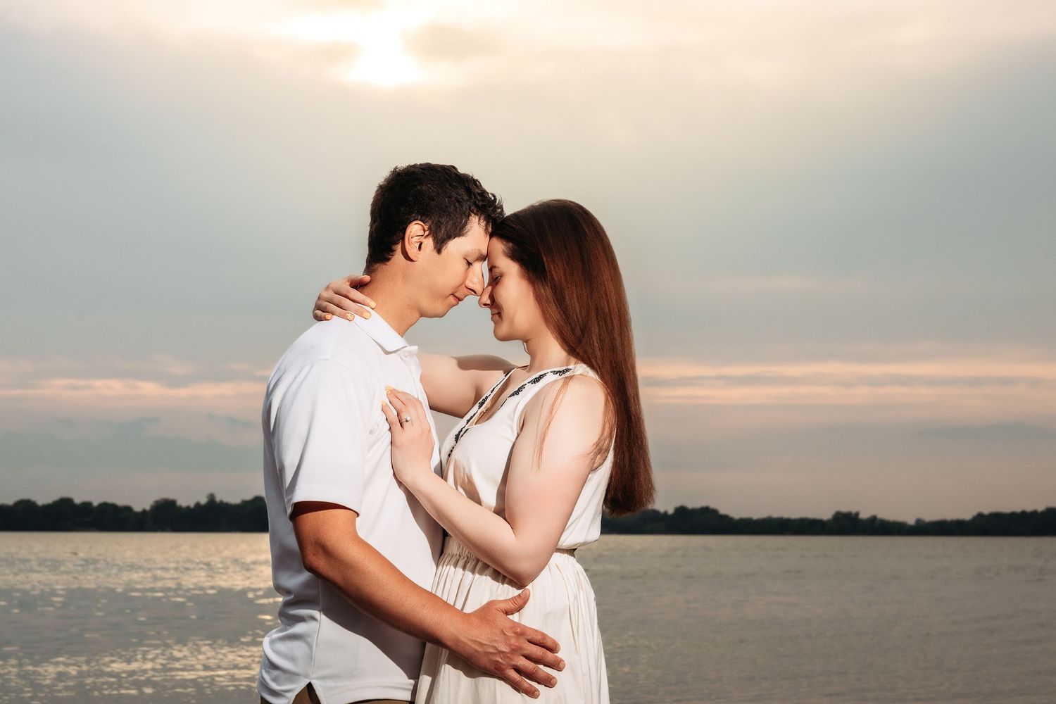 Two people share an intimate moment against a beautiful sunset over calm waters.